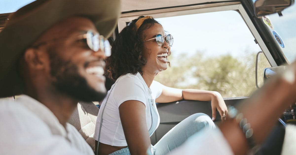 Casal sorridente dirigindo um carro, transmitindo alegria e felicidade durante a viagem.