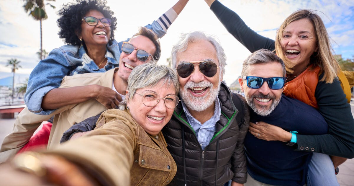 Um grupo de pessoas sorrindo e posando para tirar uma selfie em um ambiente descontraído.