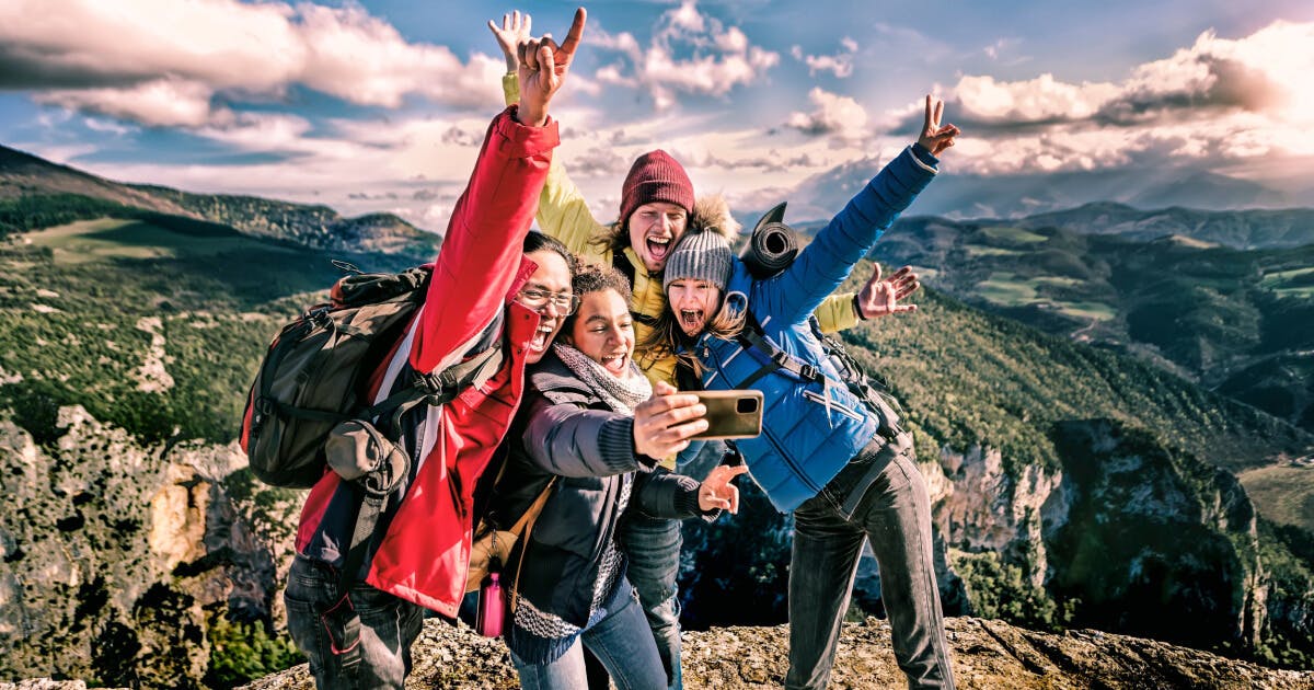 Três pessoas tirando uma selfie no topo de uma montanha, sorrindo e aproveitando a vista deslumbrante ao redor.