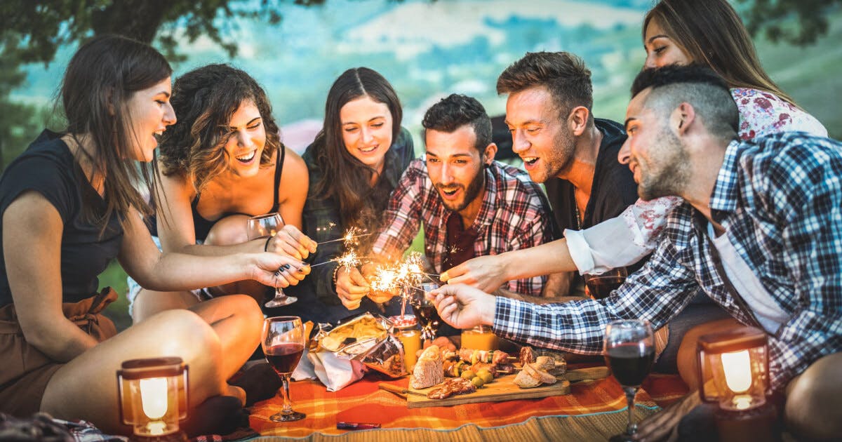 Grupo de amigos se divertindo em um piquenique, acendendo fogos de artifício e celebrando juntos ao ar livre.