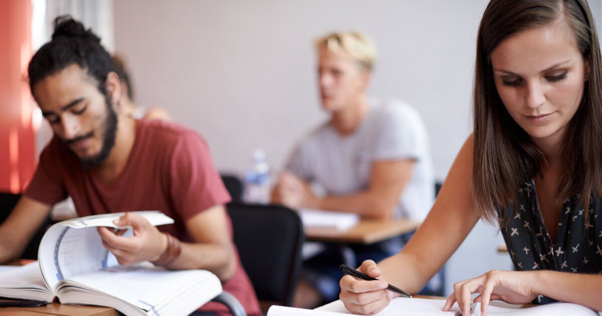 Grupo de estudantes concentrados em seus estudos dentro de uma sala de aula, rodeados por livros e materiais escolares.