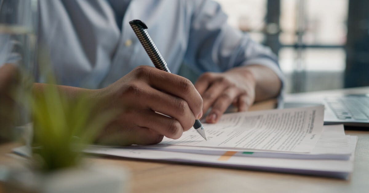 Homem assinando documentos em uma mesa, concentrado em suas tarefas administrativas.