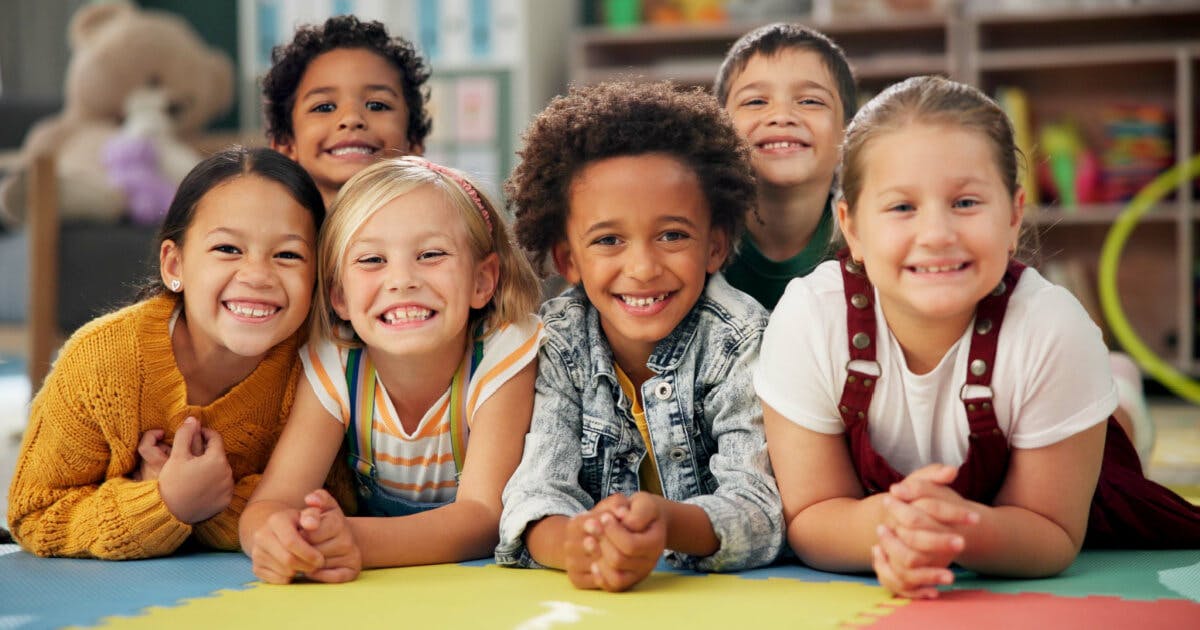 Grupo de crianças sorrindo e deitadas no chão, transmitindo alegria e diversão em um momento de brincadeira.