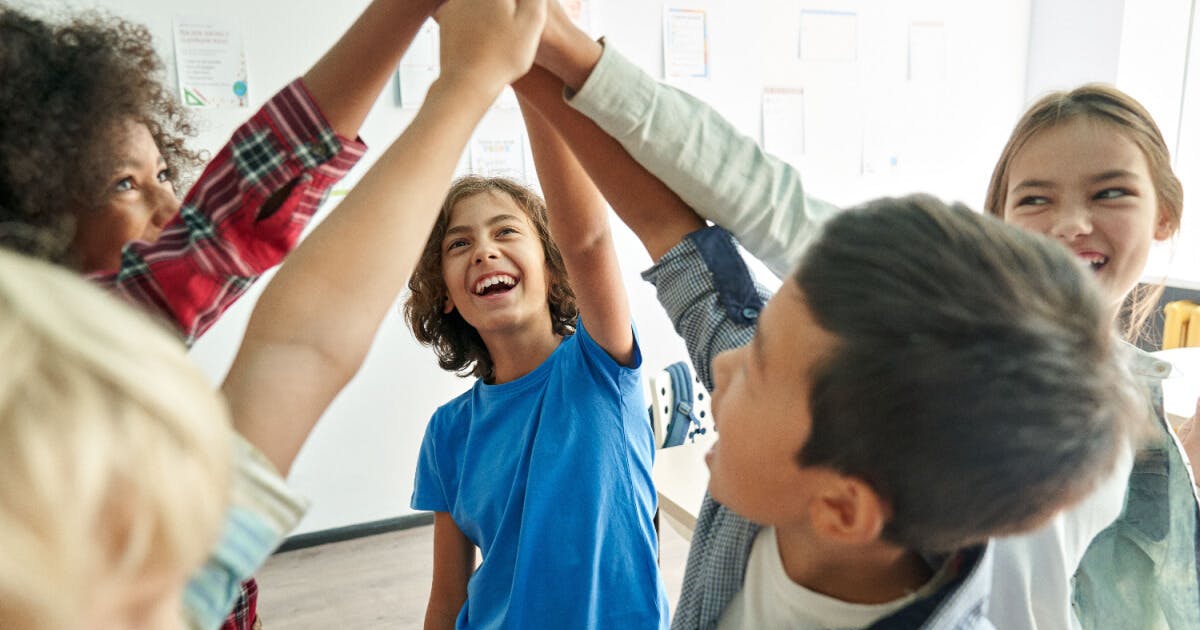 Grupo de crianças de mãos dadas em uma sala de aula, simbolizando união e amizade entre os alunos.