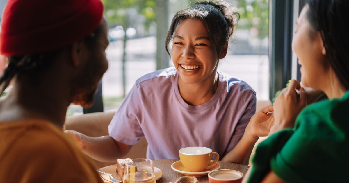 Três pessoas sentadas à mesa, desfrutando de café e comida em um ambiente acolhedor.