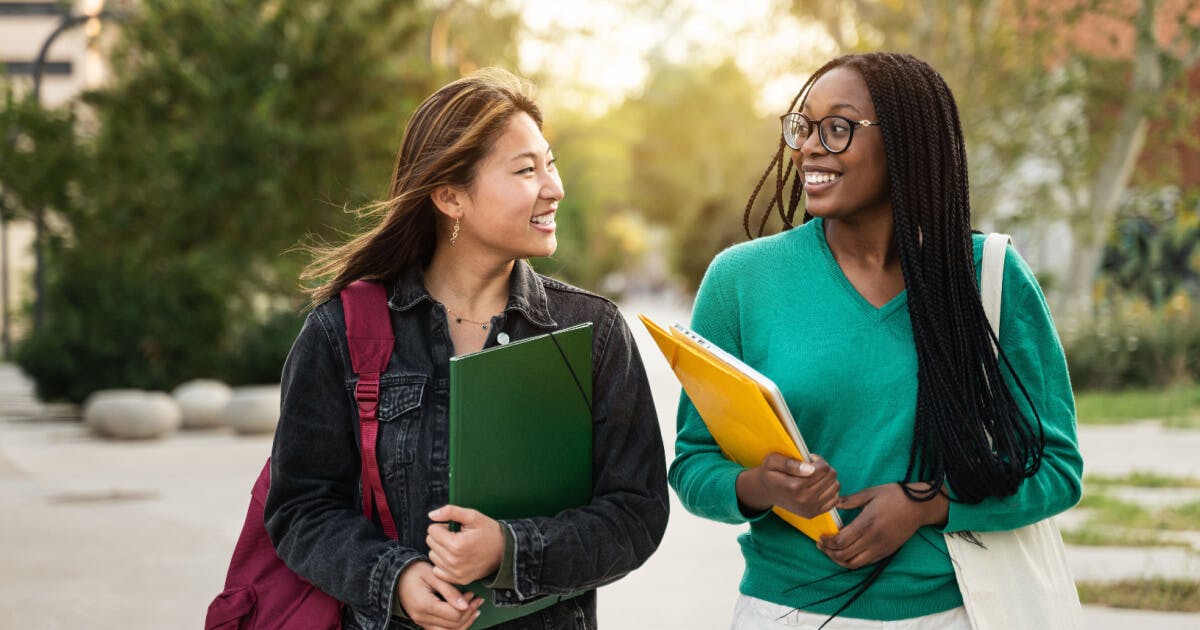 Duas estudantes caminhando juntas pelo campus, demonstrando amizade e colaboração acadêmica.