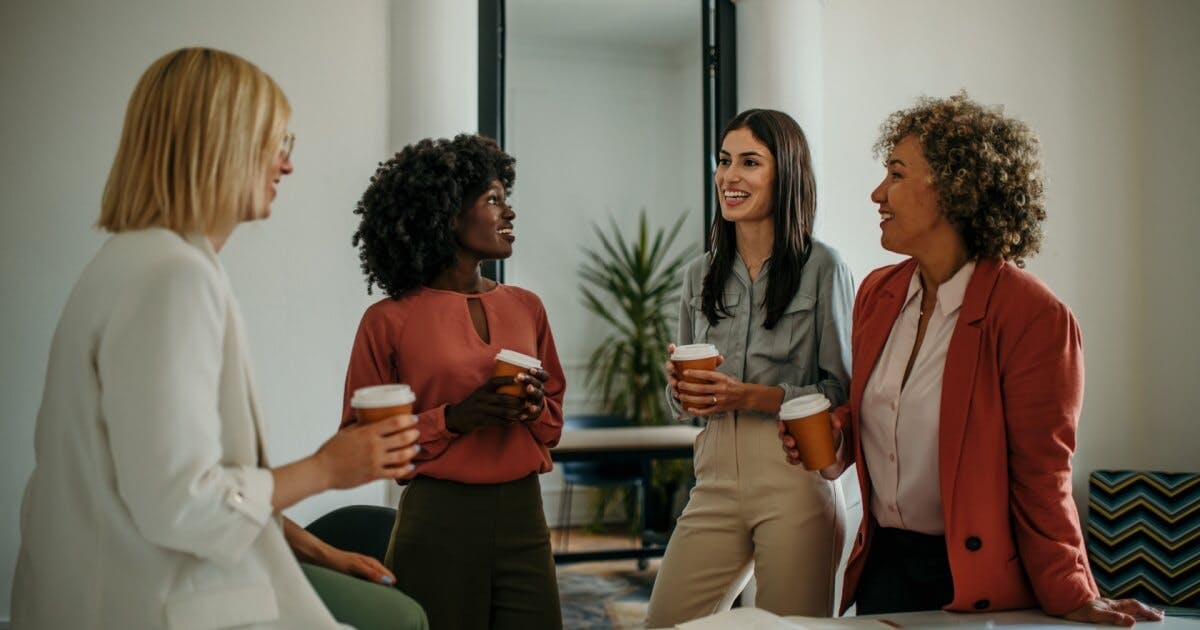 4 mulheres conversando e cada uma com um copo de café na mão.