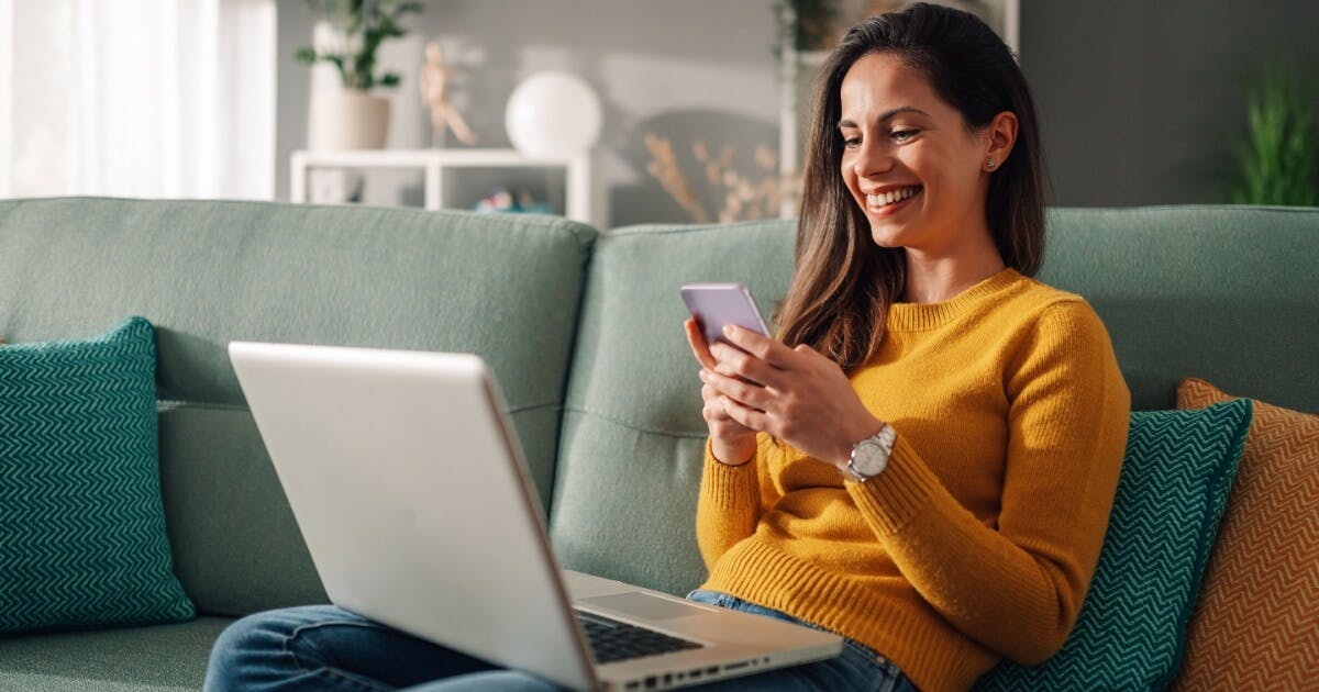 Uma mulher sentada no sofá, utilizando seu smartphone com atenção e conforto.