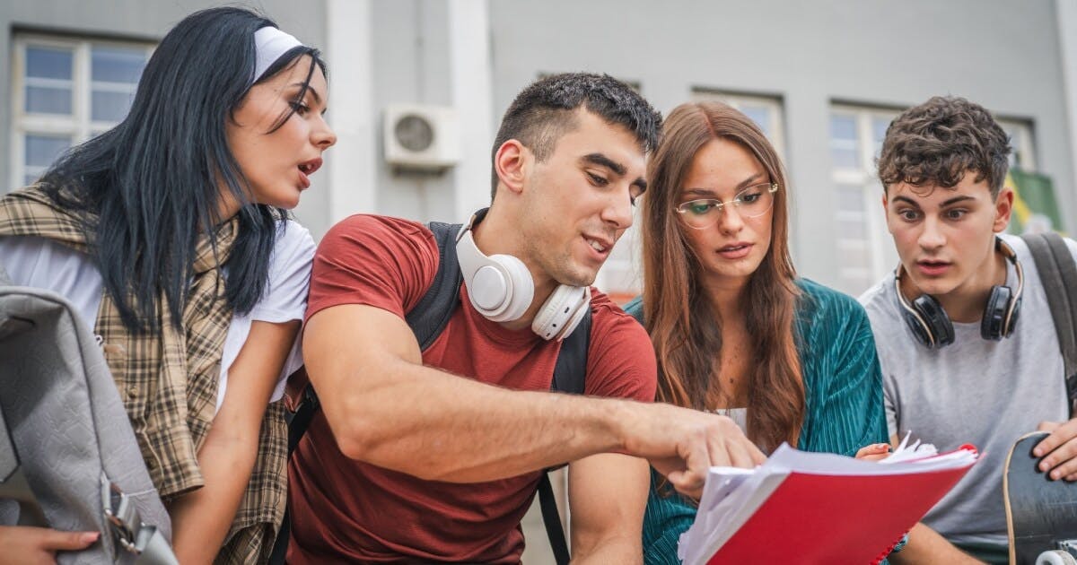 Quatro jovens observando um livro, demonstrando interesse e curiosidade em um ambiente de aprendizado.