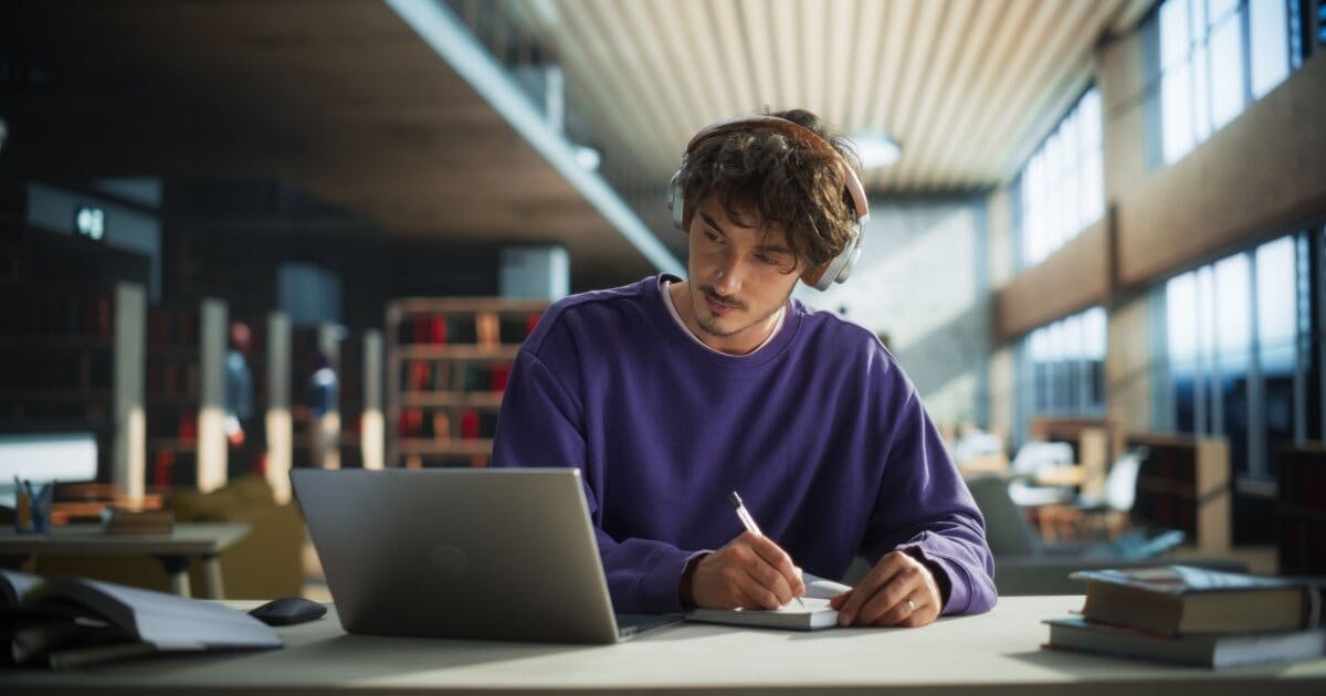 Homem com camisa roxa sentado à mesa, utilizando um laptop.