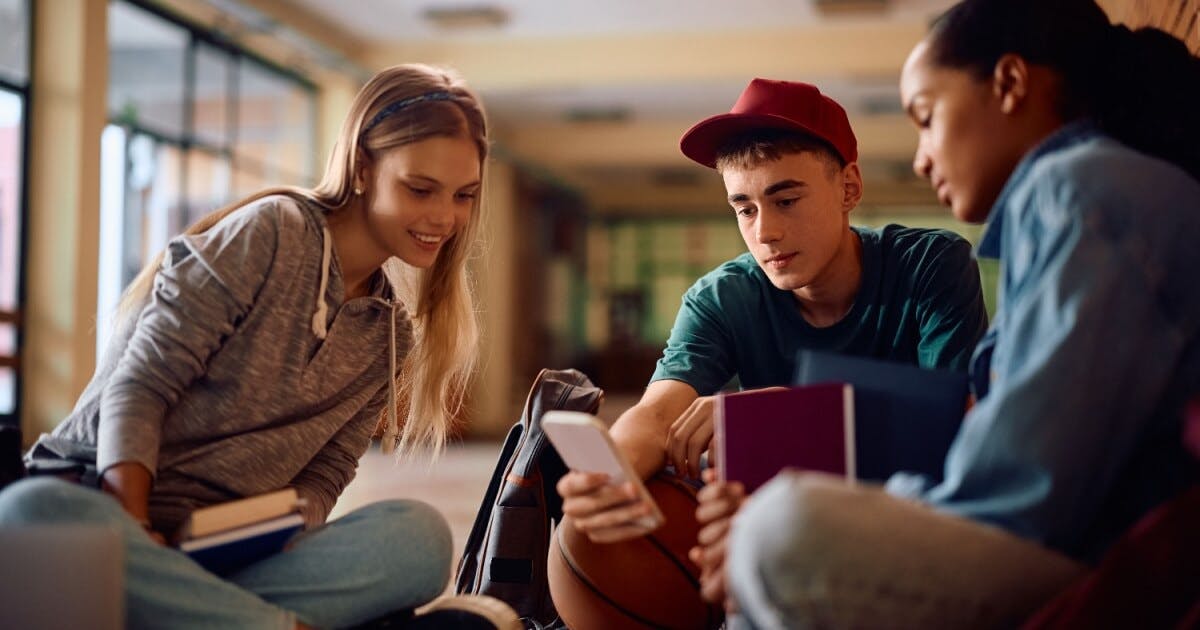 Três jovens sentados no chão, observando atentamente um celular.