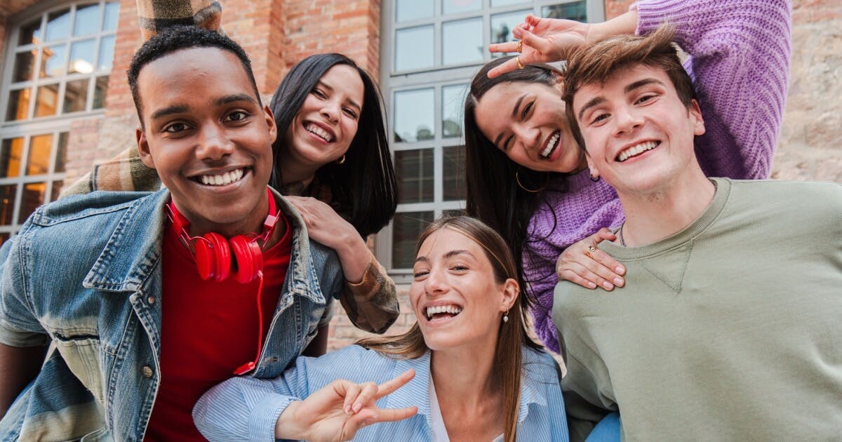 Grupo de jovens sorrindo e posando juntos para uma foto, transmitindo alegria e amizade.