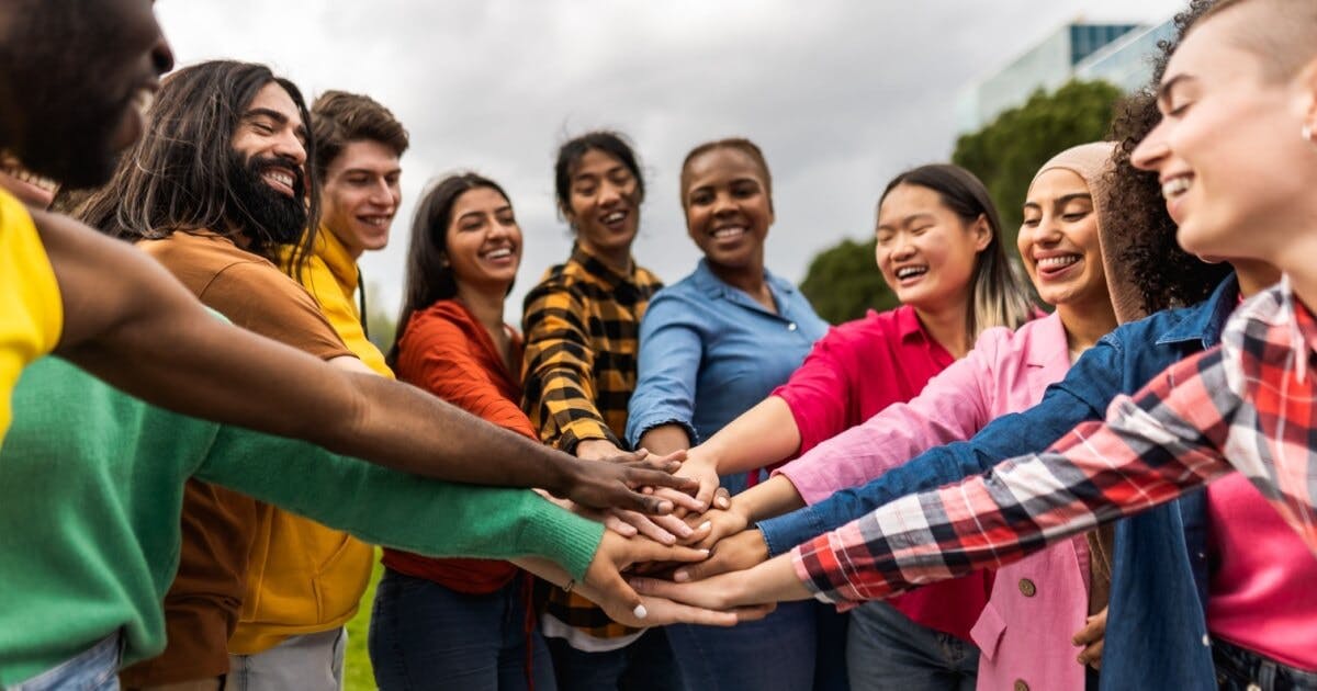 Pessoas de diferentes culturas e etnias sorrindo e com as mãos juntas.