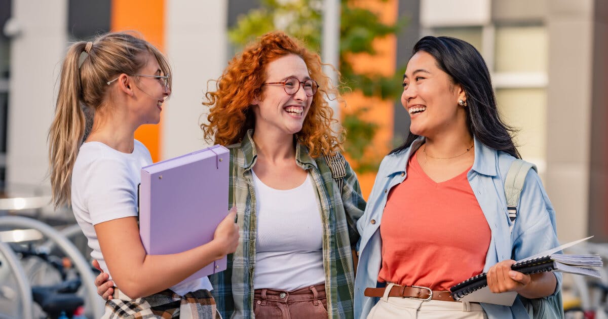 Três estudantes conversando e sorrindo, demonstrando amizade e interação positiva em um ambiente acadêmico.