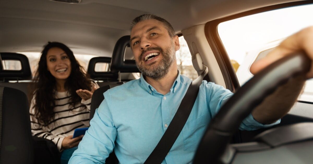 Uma mulher e um homem conversando dentro do carro. Ele está dirigindo e ela no banco de trás.