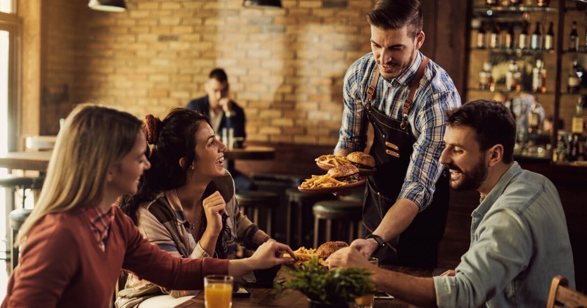 Três pessoas sendo servidas na mesa por um garçom em uma restaurante.