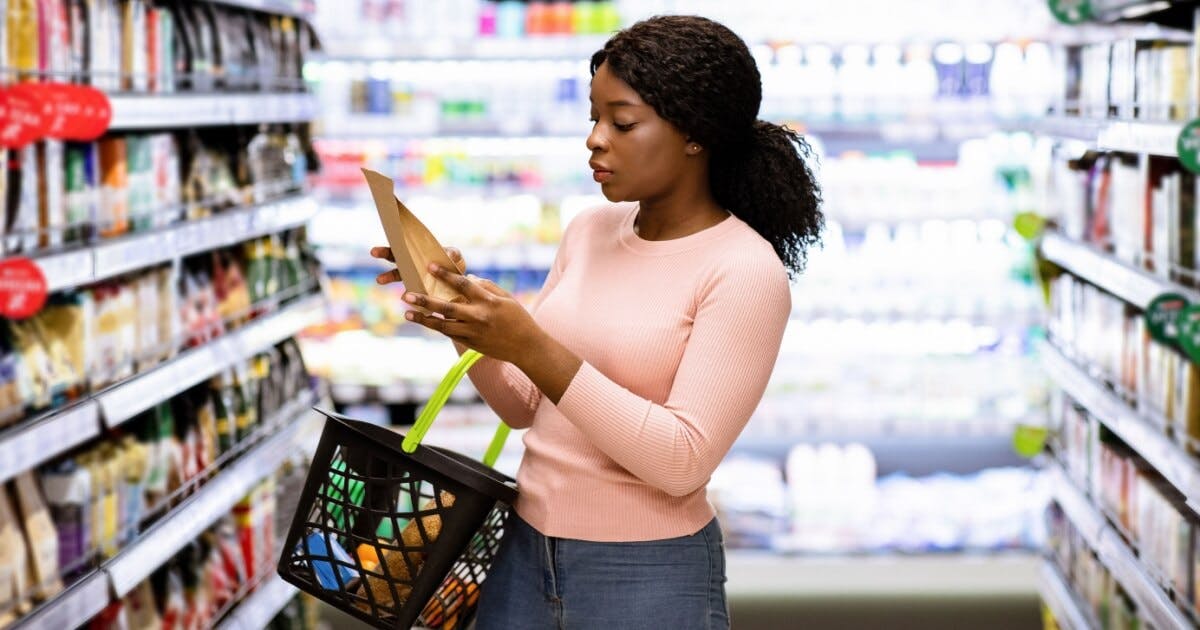 Mulher com uma cesta de compras e um pacote na mão no supermercado.