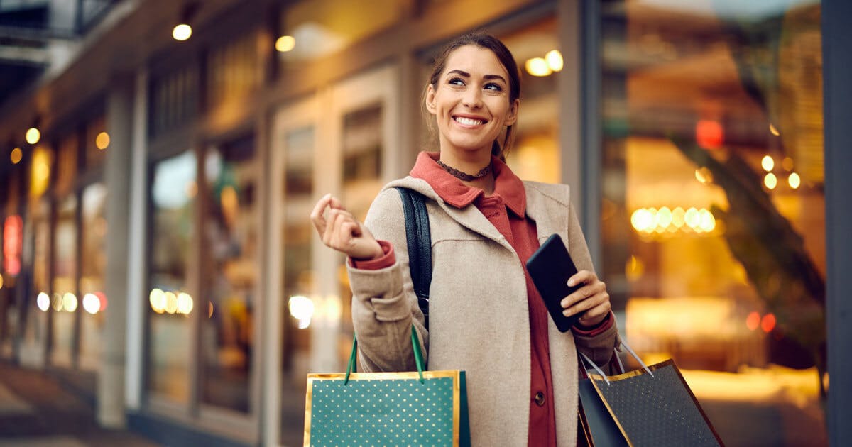 Uma mulher segurando sacolas de compras enquanto olha para o seu telefone.