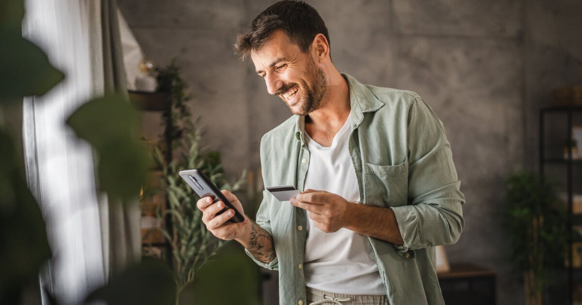 Homem utilizando seu smartphone em casa, concentrado na tela enquanto está em um ambiente doméstico confortável.