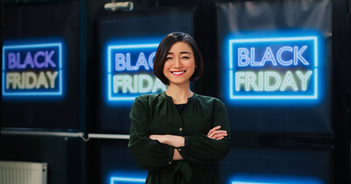 Uma mulher em pé diante de placas de Black Friday, com expressões de entusiasmo e expectativa nas compras.