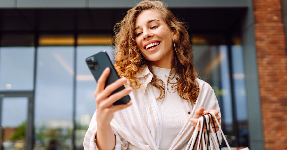 Uma mulher segurando sacolas de compras enquanto olha para o seu telefone.