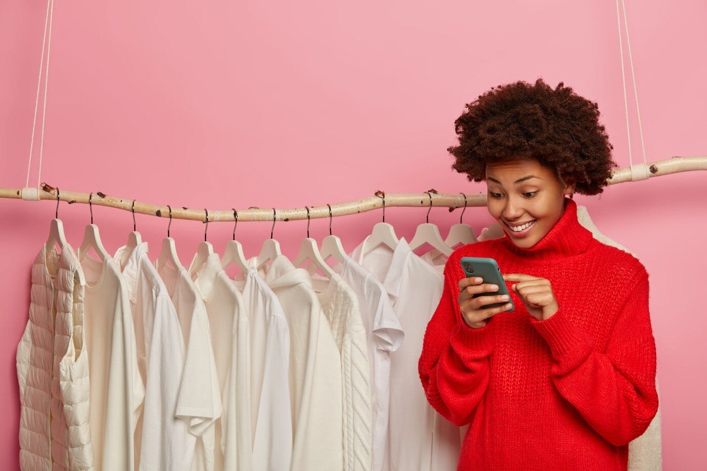 Mulher usando o celular com uma arara de roupa no fundo