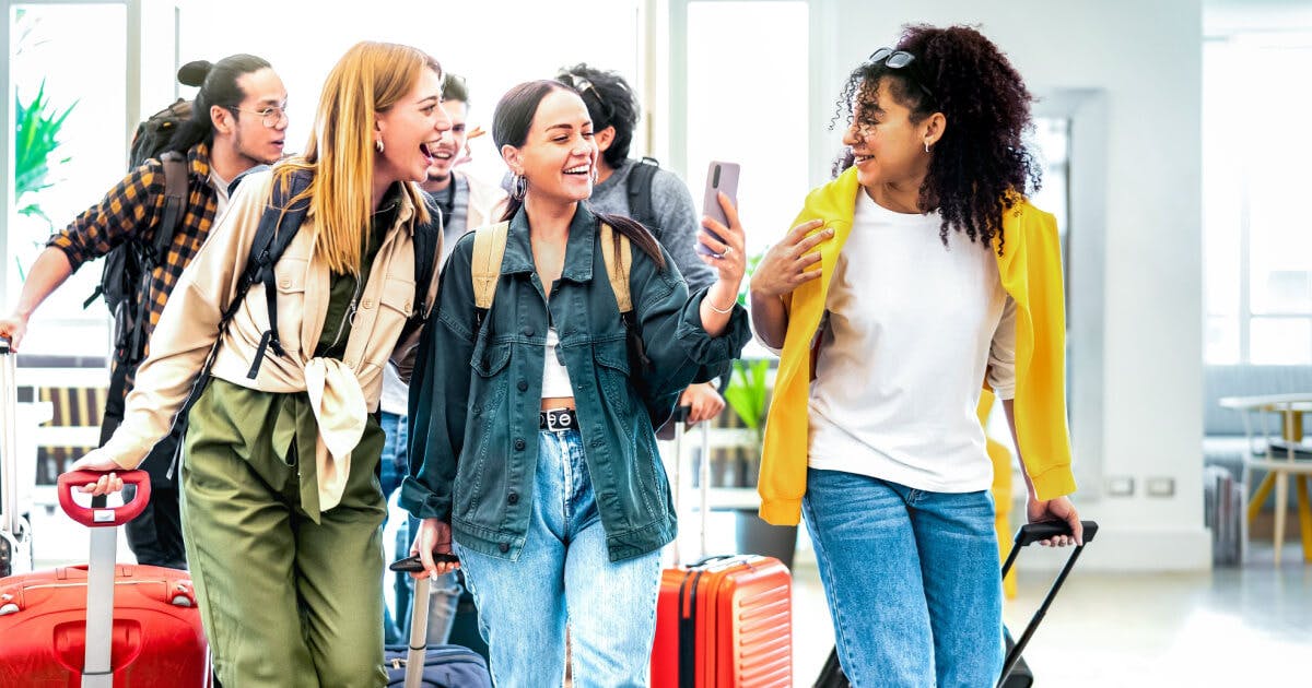 Grupo de jovens mulheres com malas e um homem, prontos para embarcar em uma viagem.