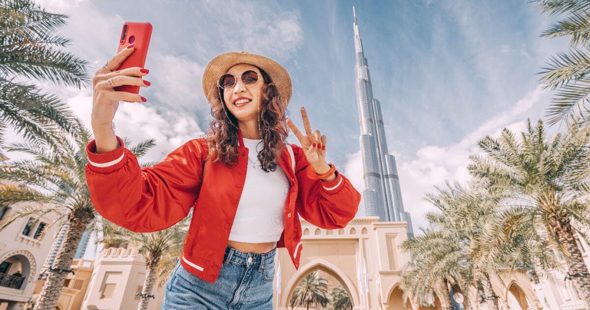 Mulher tirando selfie com o Burj Khalifa ao fundo, em Dubai, capturando um momento icônico da cidade.