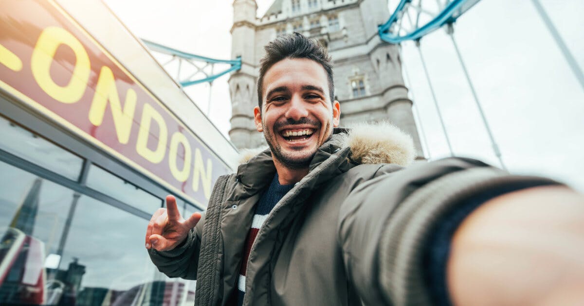 Homem tirando selfie em frente à Tower Bridge, em Londres, com a famosa ponte ao fundo.