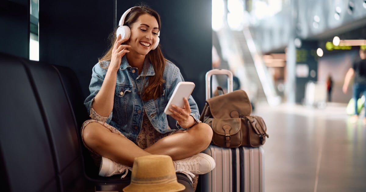 Uma mulher sentada em um banco, com uma mala ao lado e fones de ouvido, desfrutando de um momento de tranquilidade.