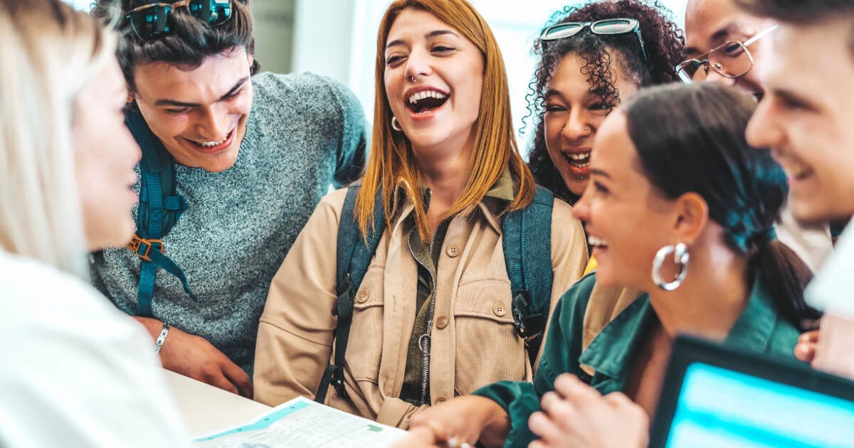 Grupo de jovens sorrindo e rindo enquanto interagem com um computador, transmitindo alegria e camaradagem.