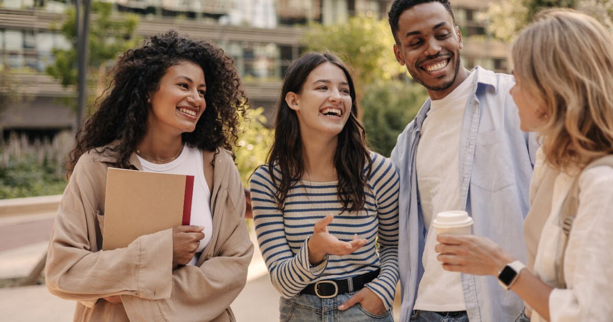 Quatro jovens conversando e sorrindo juntos, demonstrando amizade e alegria em um ambiente descontraído.