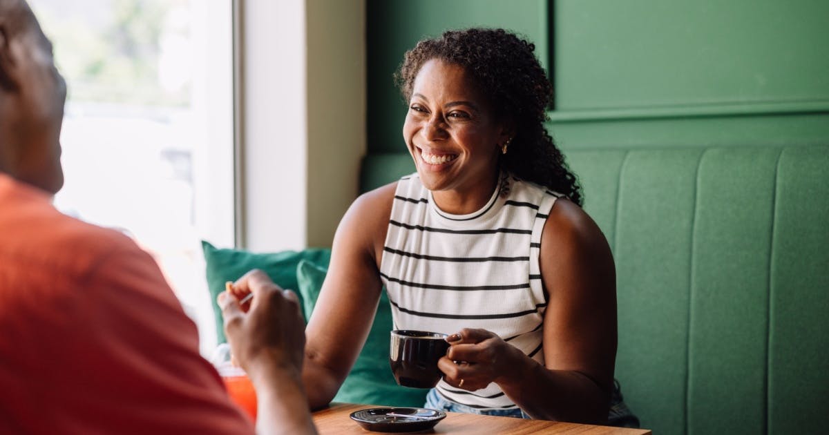 Mulher sorrindo para um homem com um café na mão.