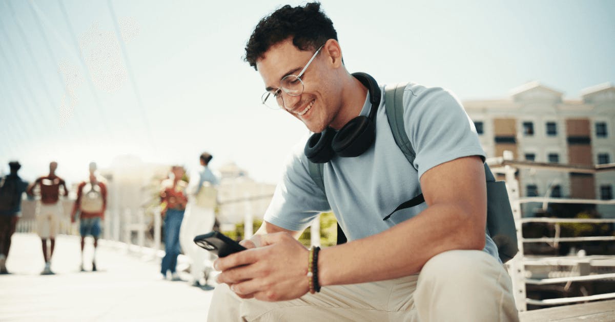 Homem com fones de ouvido e óculos sentado em uma ponte, olhando para o horizonte.