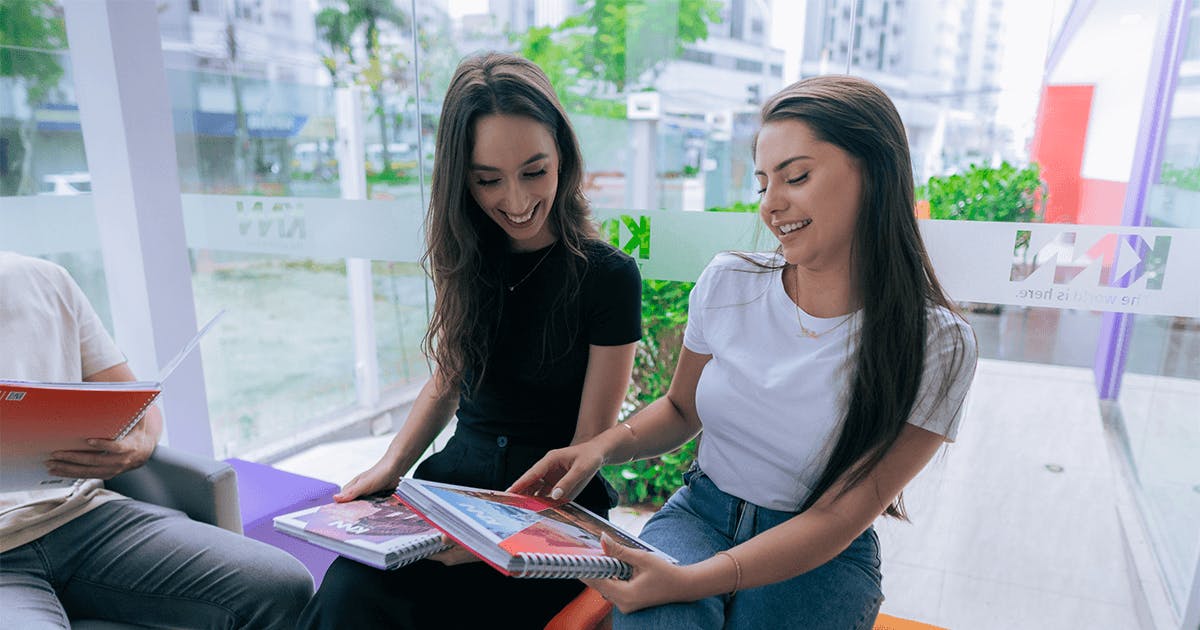Duas jovens sentadas no sofá, usando um laptop e conversando animadamente.