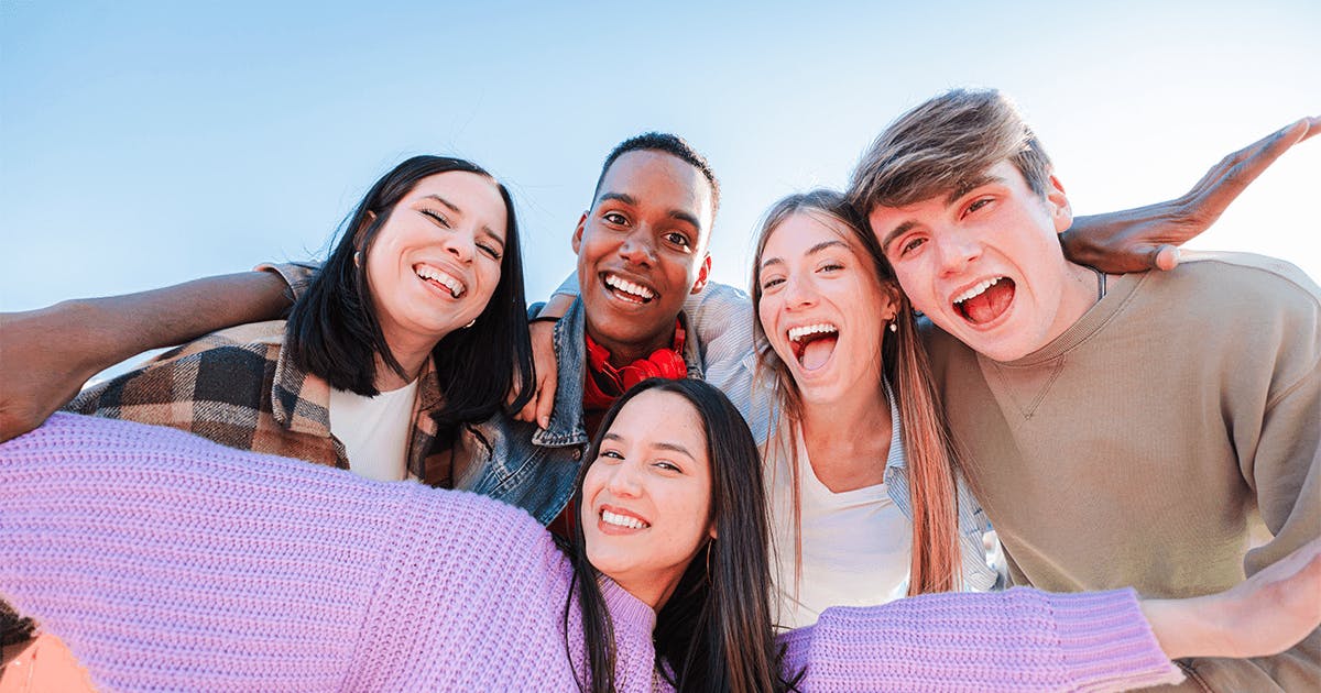 Grupo de jovens sorrindo enquanto tiram uma selfie juntos.