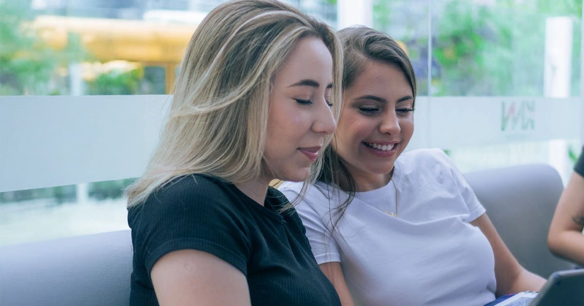 Duas alunas KNN sorrindo enquanto estudam juntas em ambiente moderno