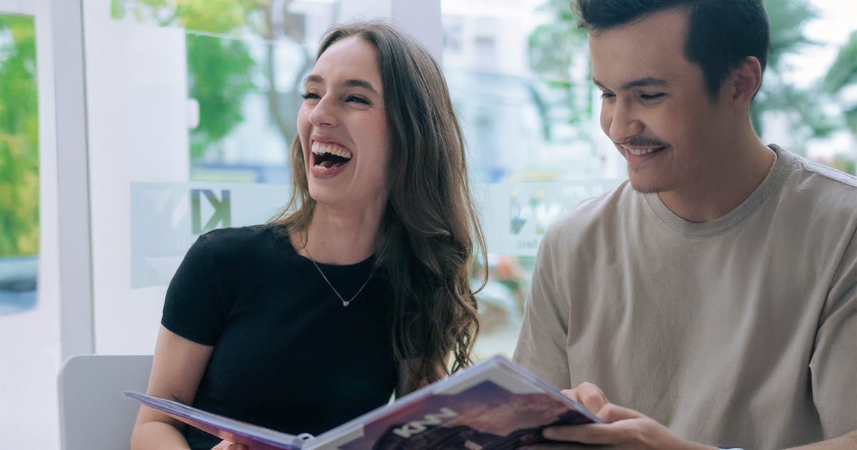 Dois alunos KNN sorrindo enquanto estudam juntos com material didático