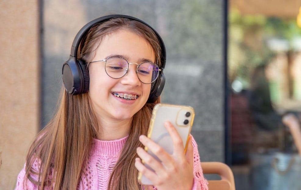 menina sorrindo com fones de ouvido e um celular na mão