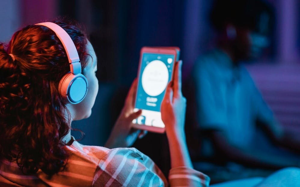 Mulher de costas escutando algo nos fones de ouvido com um tablet na mão
