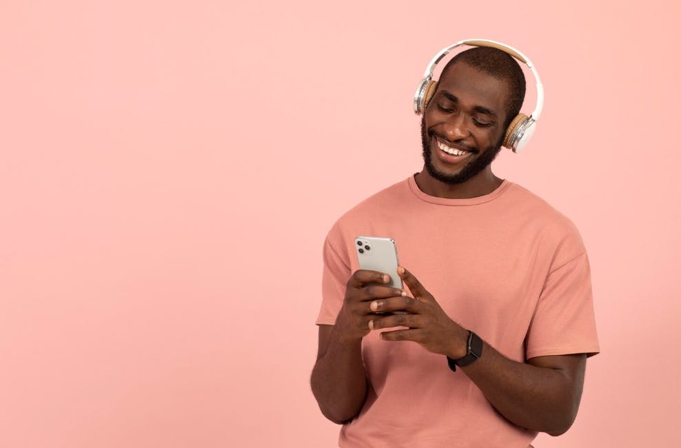 Homem segurando um celular e cm fones de ouvido em um fundo rosa