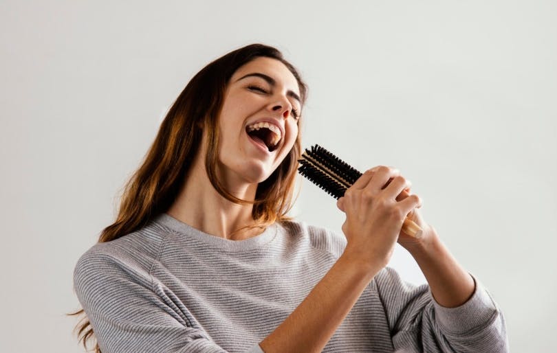 Mulher cantando com uma escpva de cabelo
