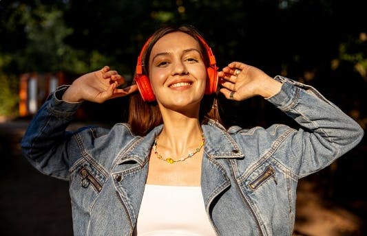 Mulher com fones de ouvido em um parque, de olhos fechados, curtindo música em clima relaxante.