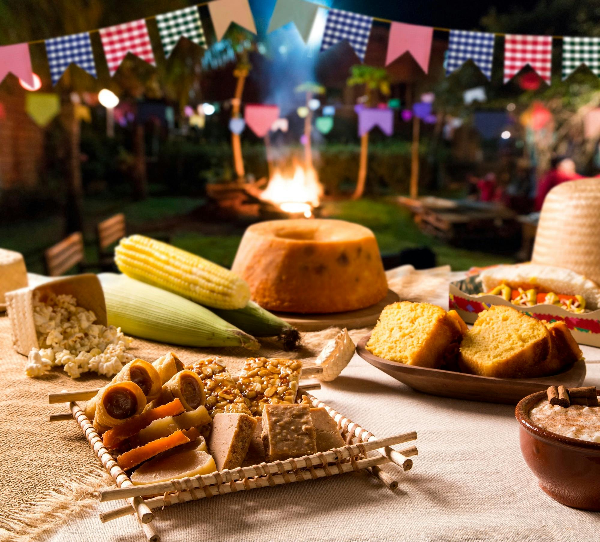 Mesa com bolo, milho e comidas típicas de festas juninas.