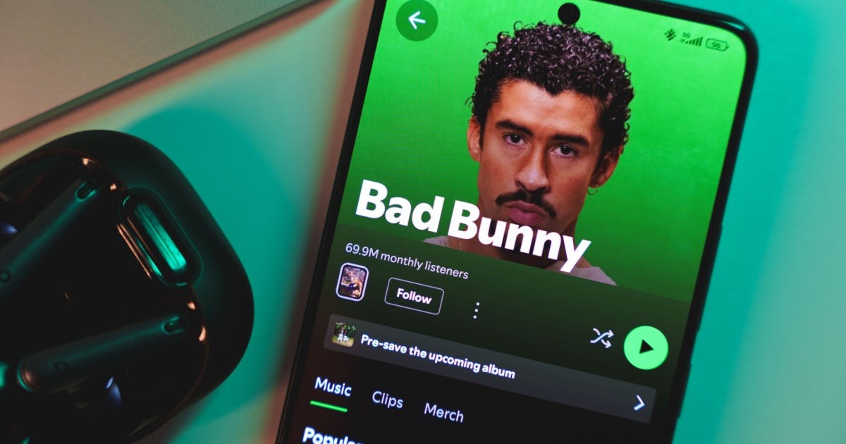 Um fone de ouvido e um smartphone com a capa do cantor Bad Bunny no aplicativo Spotify.