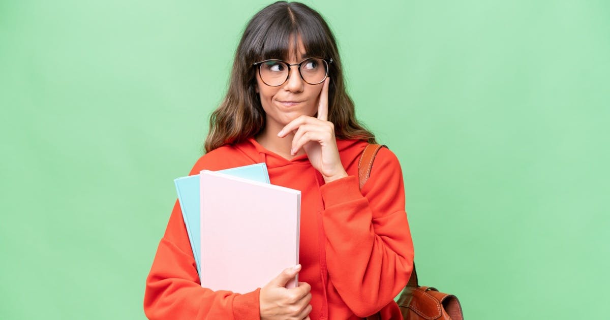 Mulher de óculos, com dois livros na mão, moletom laranja e expressão de dúvida.