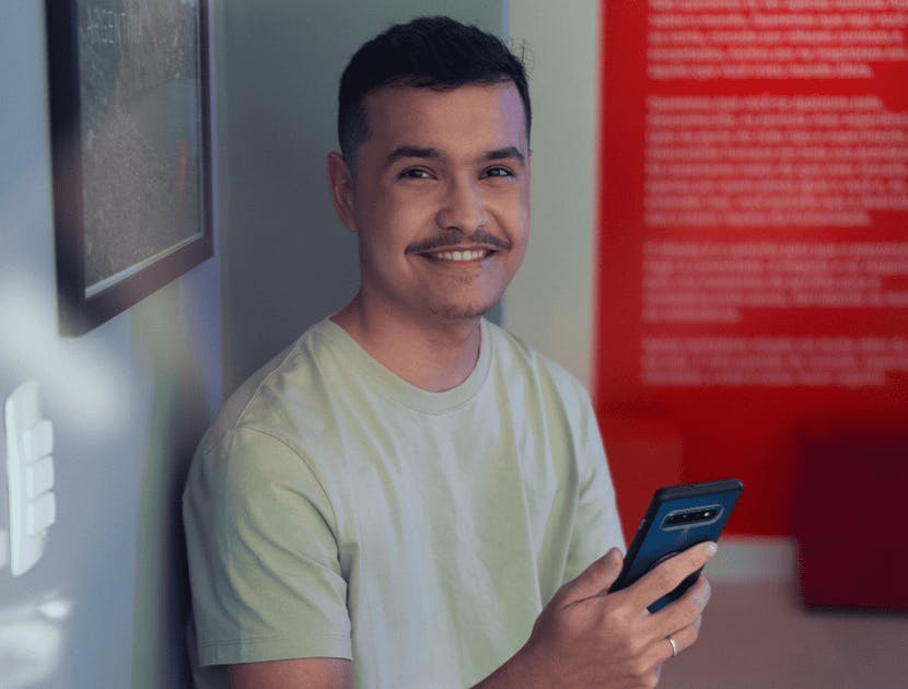 Homem sorrindo, olhando para a foto e com o celular na mão.