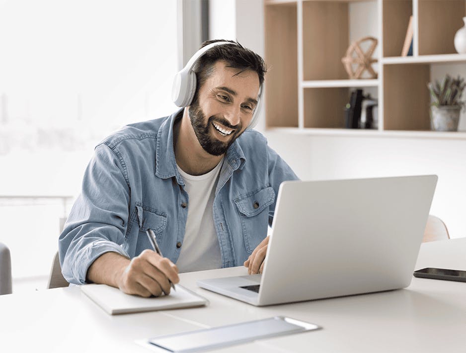 Um homem com camisa azul está sentado à mesa, usando um laptop.