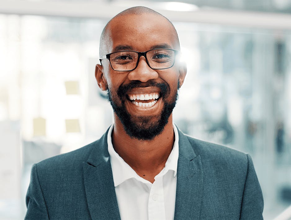 Homem sorridente, usando terno e óculos, posando com um ar confiante.