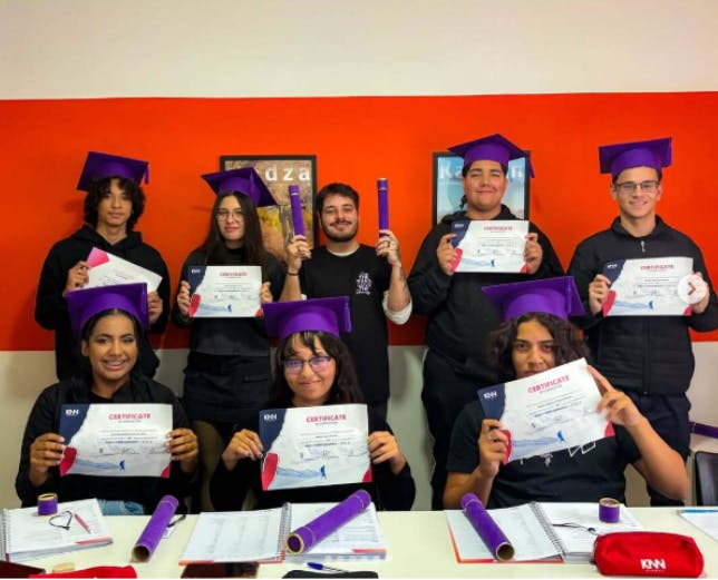 Turma da KNN Idiomas no dia da formatura, com certificados em mãos e a toga roxa na cabeça.